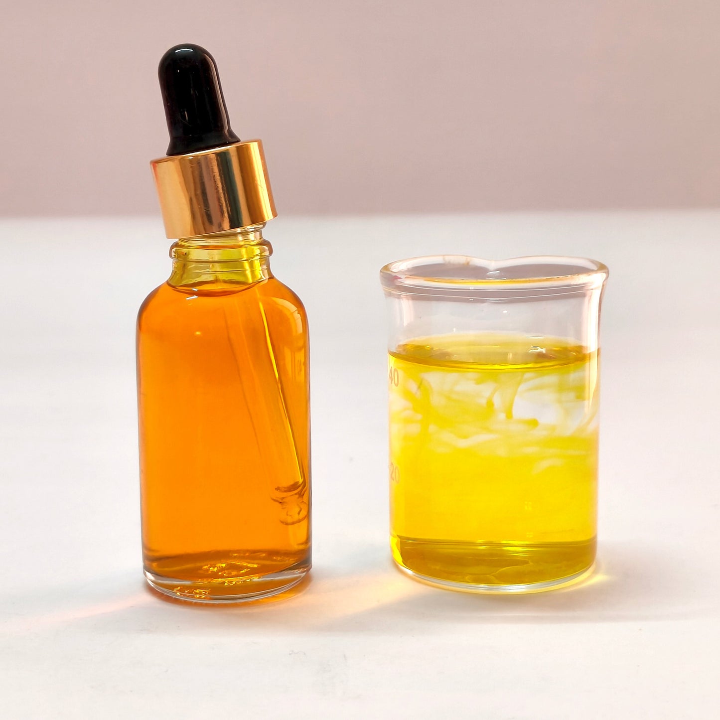 Glass dropper bottle and beaker filled with yellow liquid on a white background