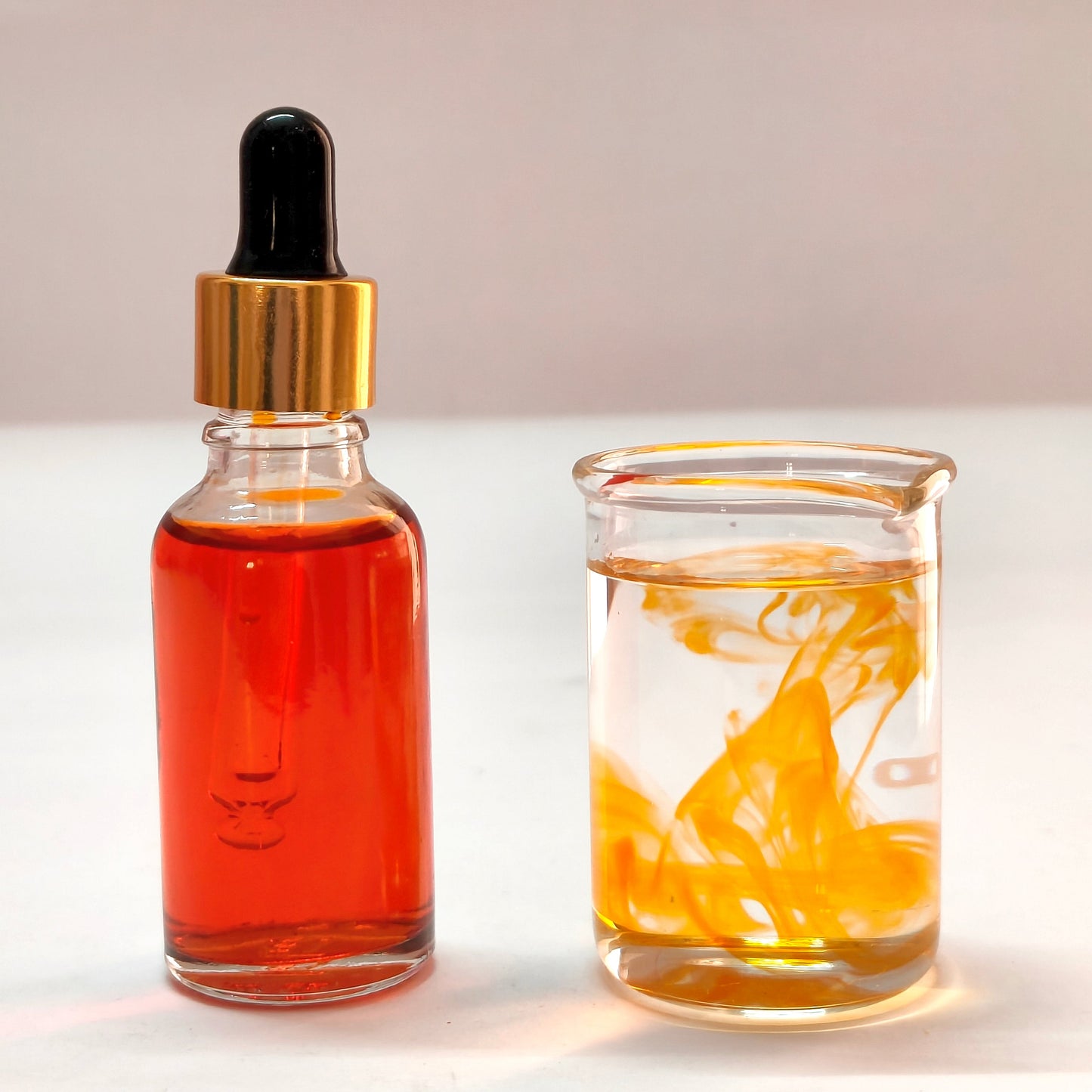 Glass dropper bottle with amber liquid next to a glass jar with yellow liquid on a light background