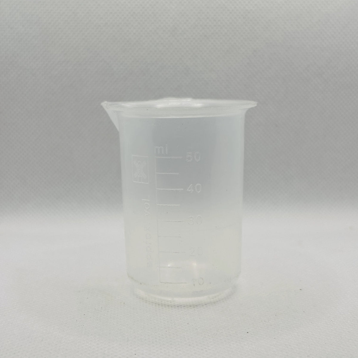 A small translucent plastic beaker with printed measurement markings in milliliters, shown against a light gray textured background.