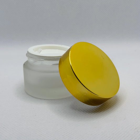 A frosted glass cosmetic jar with a white screw-on lid removed and leaning against the jar on a light gray textured background.