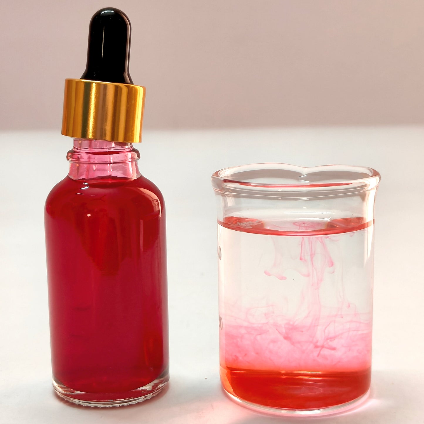 Bottle of red liquid with dropper and glass container filled with red liquid on a light background