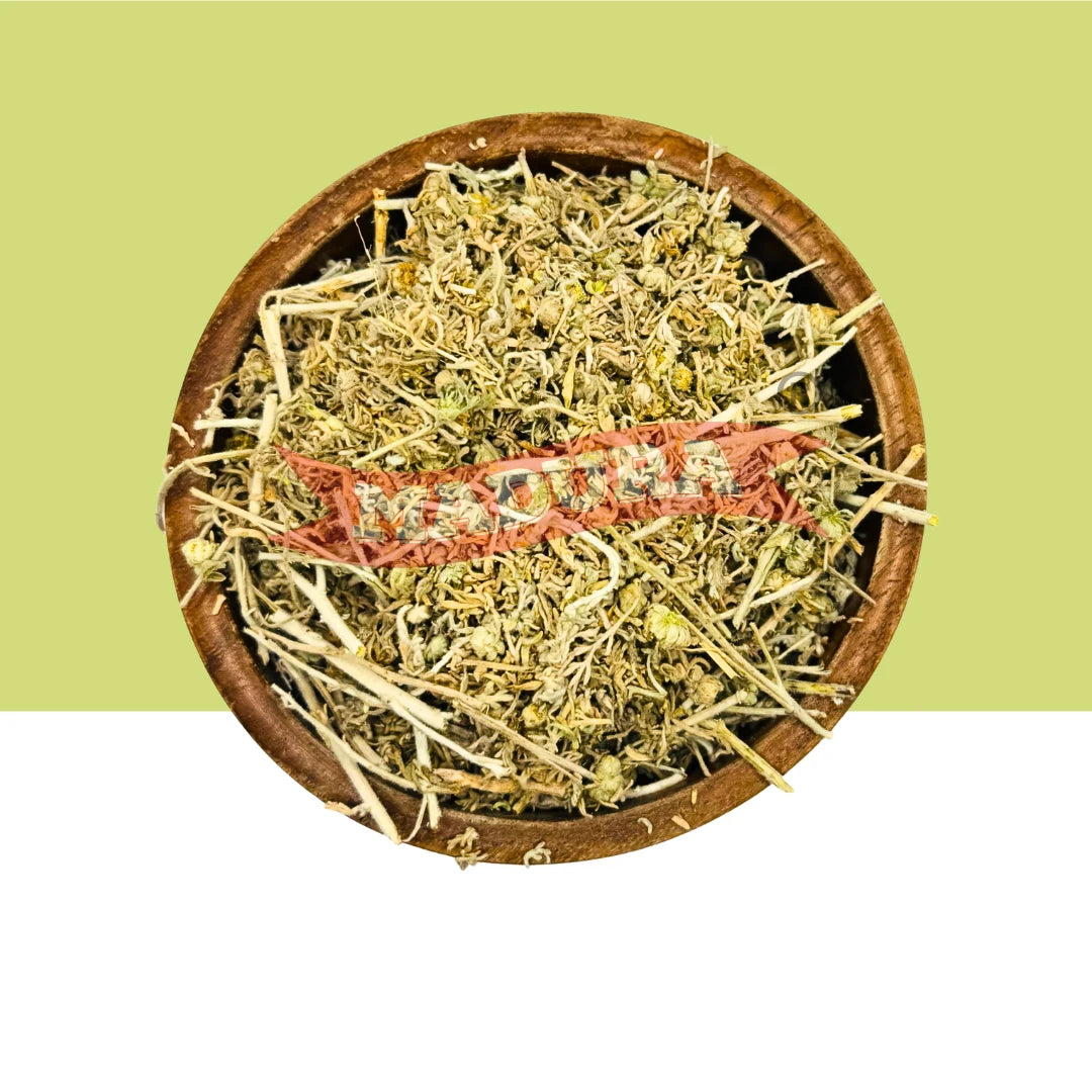 A round wooden bowl filled with dried herbal Marikolunthu, featuring pale green and beige botanicals with a prominent pinkish-red strip across the center, set against a split light green and white background.