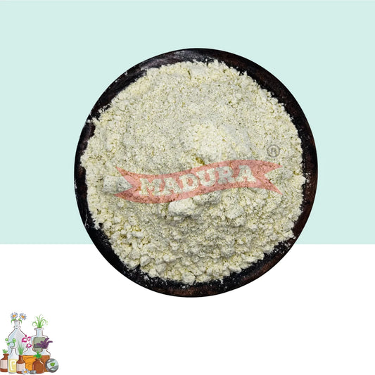 A pile of pale off-white powder, likely milk powder, displayed in a round dark bowl. The image has a split background with a light mint green top half and a white bottom half, featuring a red 'MADURA' banner watermark across the center and a small decorative logo in the bottom-left corner.